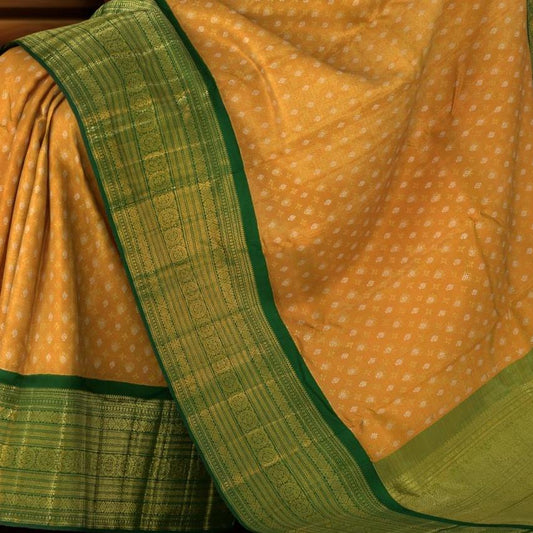 Light Orange Kanchipuram Tissue Silk Saree embossed, and intricately designed silver and gold butta on the body with leaf green contrast border and annam, grand, kuyil kan designs in pallu